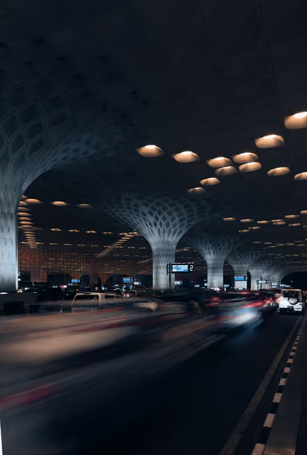 Airport terminal departure roadway at night under a canopy with mushroom-shaped columns, recessed lights, and motion-blurred cars