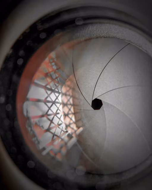 Close-up of a camera lens aperture blades forming a hexagonal opening, with a blurred lattice structure reflected in the glass.