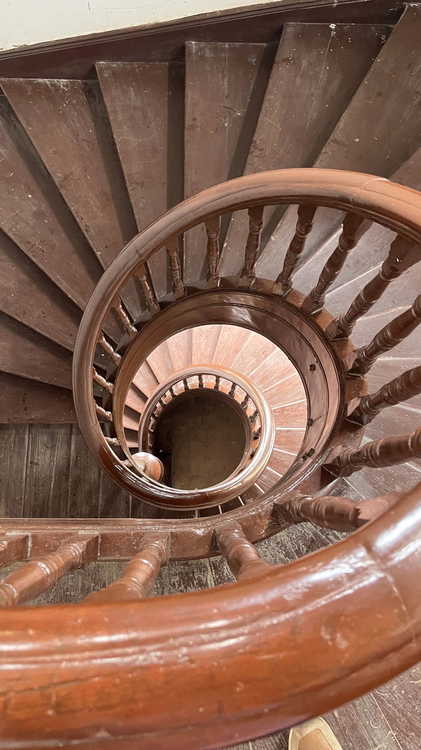 Looking down the centre of a wooden spiral staircase with turned balusters and a polished handrail curving through several floors