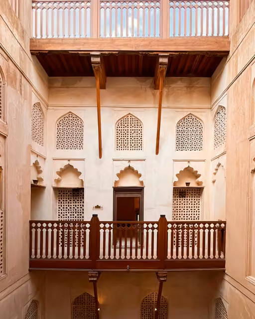 Interior courtyard of a traditional fort with carved lattice windows, arched niches, wooden balconies, and diagonal wooden support beams overhead.